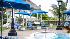 A pool area with lounge chairs and umbrellas, a gazebo, and a hot tub.