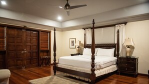 A four-poster bed with a wooden frame and white bedding, a nightstand with a lamp, a wooden floor, and a ceiling fan.