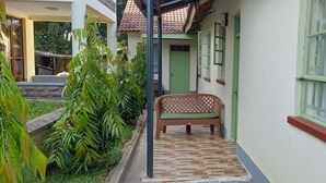 Un estrecho pasillo exterior con un banco, una puerta verde y una ventana con rejas.