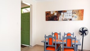 Un comedor con una mesa y sillas, una puerta verde, un ventilador y una obra de arte colgada en la pared.