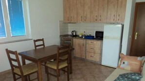 A compact kitchen with wooden cabinets, a dining table with chairs, a refrigerator, and a sofa with cushions. - Apartment 100m from sea, with covered terrace, citrus trees (Sveti Filip i Jakov)