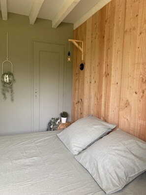A bedroom with a wooden headboard, a bed with striped bedding, a hanging light fixture, and a small plant on a woven stool. - Exceptional promotion for the month of September magnificent villa landaise (Messanges)