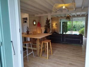 A modern kitchen with a wooden table and stools, a surfboard decoration, and a view of greenery outside. - Exceptional promotion for the month of September magnificent villa landaise (Messanges)