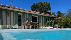 A poolside view of a building with a tiled roof, a covered patio area, and a clear blue pool.