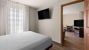 Hotellihuone, jossa on sänky, seinälle asennettu televisio ja puulattia.