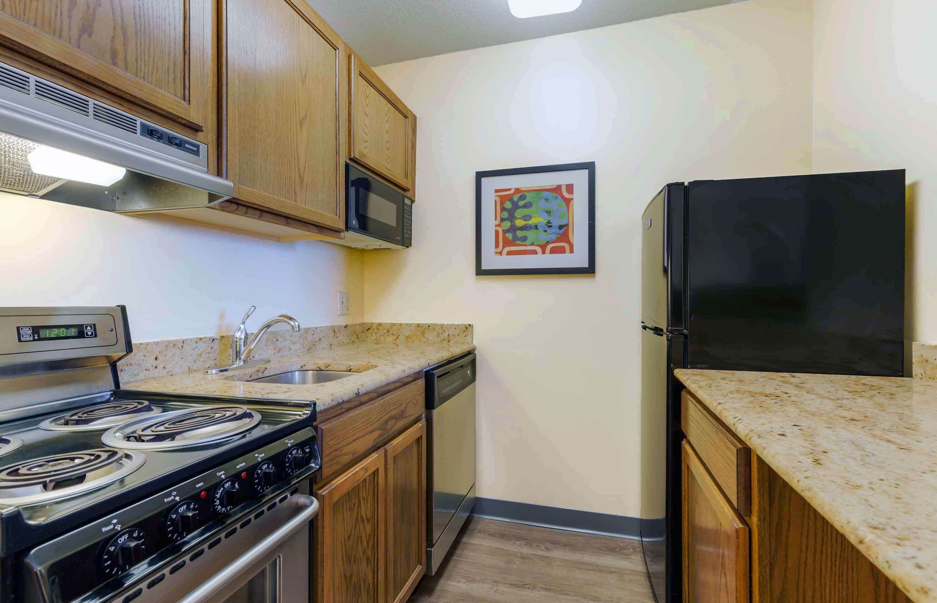Una cocina con armarios de madera, estufa de acero inoxidable, microondas, lavavajillas y un refrigerador negro.