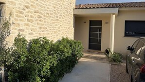 A house with a stone facade, a tiled roof, a black door, and a car parked in the driveway. - Beautiful villa in the south of France (Argilliers)