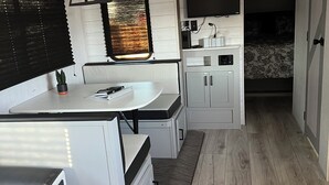 Una cocina compacta con microondas integrado, un lavamanos pequeño y una ventana con persianas.