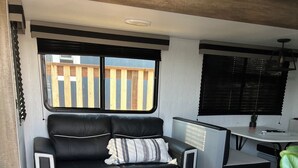 Interior compacto de una caravana con sofá de cuero negro, una pequeña mesa de comedor y una zona de kitchenette.