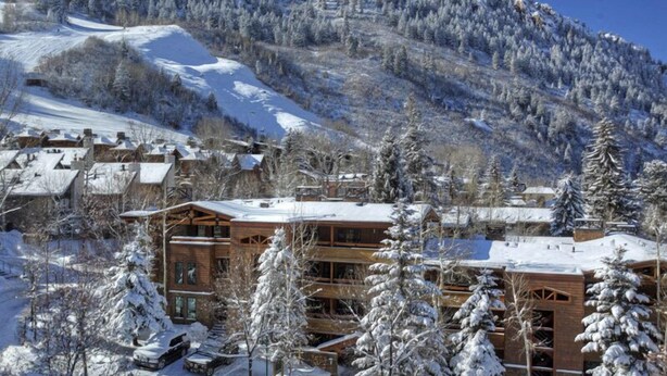 Un chalet enneigé à plusieurs étages, entouré d’arbres chargés de neige et dominé par un paysage montagneux.