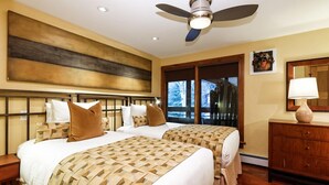 Une chambre d’hôtel avec deux lits, un ventilateur de plafond, une grande fenêtre et une armoire en bois.