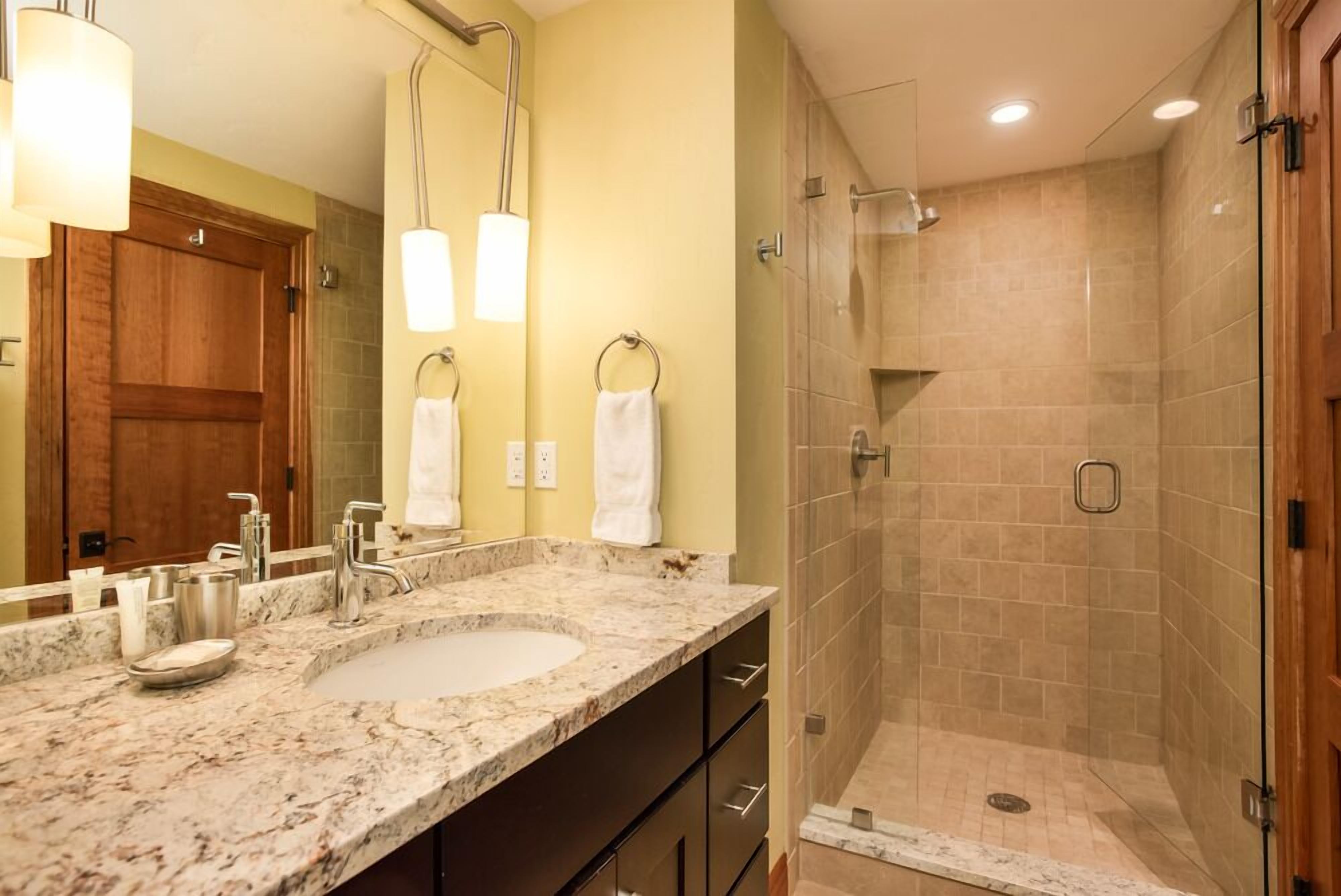 Une salle de bain avec un lavabo en marbre, deux porte-serviettes, une porte en bois et une douche séparée par une paroi de verre.