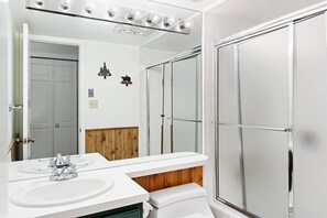 Ein Badezimmer mit weißem Waschtisch, einem großen Spiegel und einer Dusche mit Glastür.