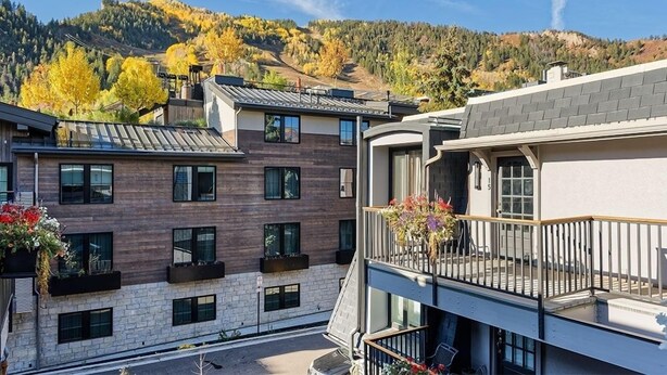 A modern multi-story building with balconies, large windows, and a view of a mountainous landscape.