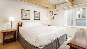 A bedroom with a large bed, wooden headboard, two bedside tables with lamps, framed pictures on the wall, and a window with a view of the outside.