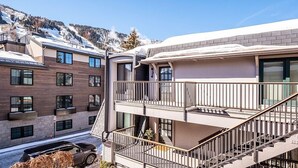 A multi-story residential building with balconies, a staircase, and a view of snow-covered mountains.
