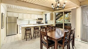 A kitchen with wooden cabinets, a stainless steel refrigerator, a central island with stools, and a chandelier.