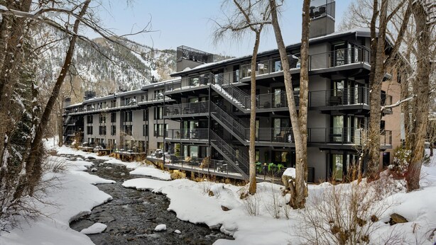 A modern multi-story building with balconies and a river in the foreground.