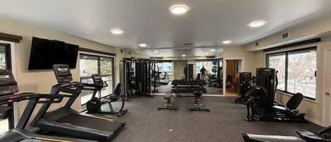 Un gimnasio con cintas de correr, máquinas de pesas y pesas libres.