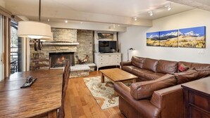 Un salon spacieux avec une cheminée, une table à manger en bois, un canapé en cuir et un téléviseur à écran plat.
