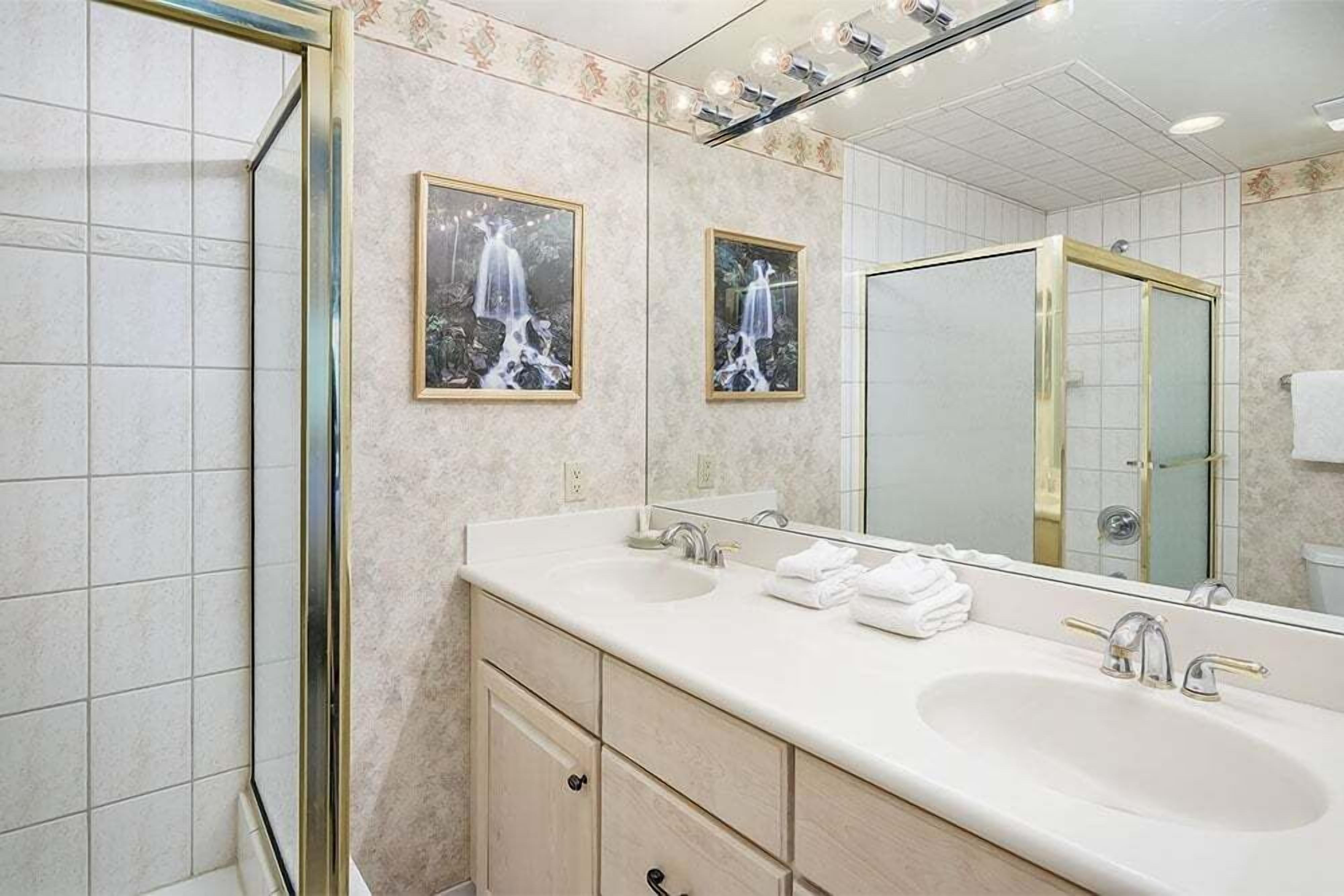 Une salle de bain avec deux lavabos, un grand miroir et des œuvres d’art encadrées accrochées au mur.