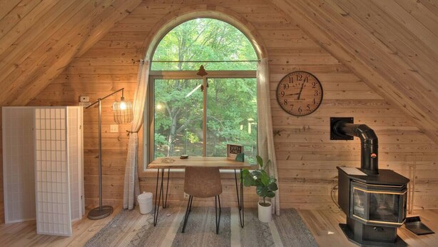 Ein gemütliches Dachzimmer mit einem großen Rundbogenfenster, einem Holzofen und einer Wanduhr.