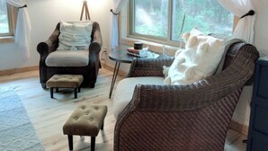 Ein gemütliches Zimmer mit Korbmöbeln, einer Lampe und Blick auf den Wald.