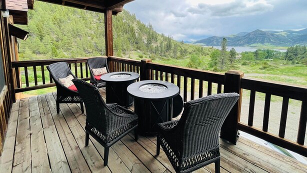 Eine Holzterrasse mit Korbstühlen und einem runden Tisch, mit Blick auf eine Berglandschaft mit einem See.