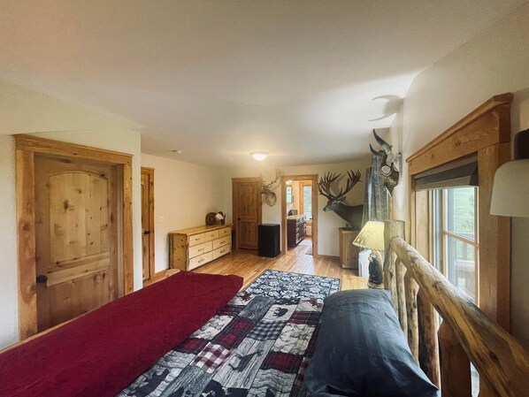 Une chambre à coucher avec un lit en bois, une couverture rouge, une courtepointe et une tête de cerf accrochée au mur.