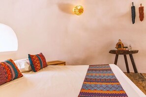 Ein Schlafzimmer mit einem Bett, Kissen, einem gemusterten Teppich, einer Wandleuchte und einem kleinen Tisch mit einem Korb.