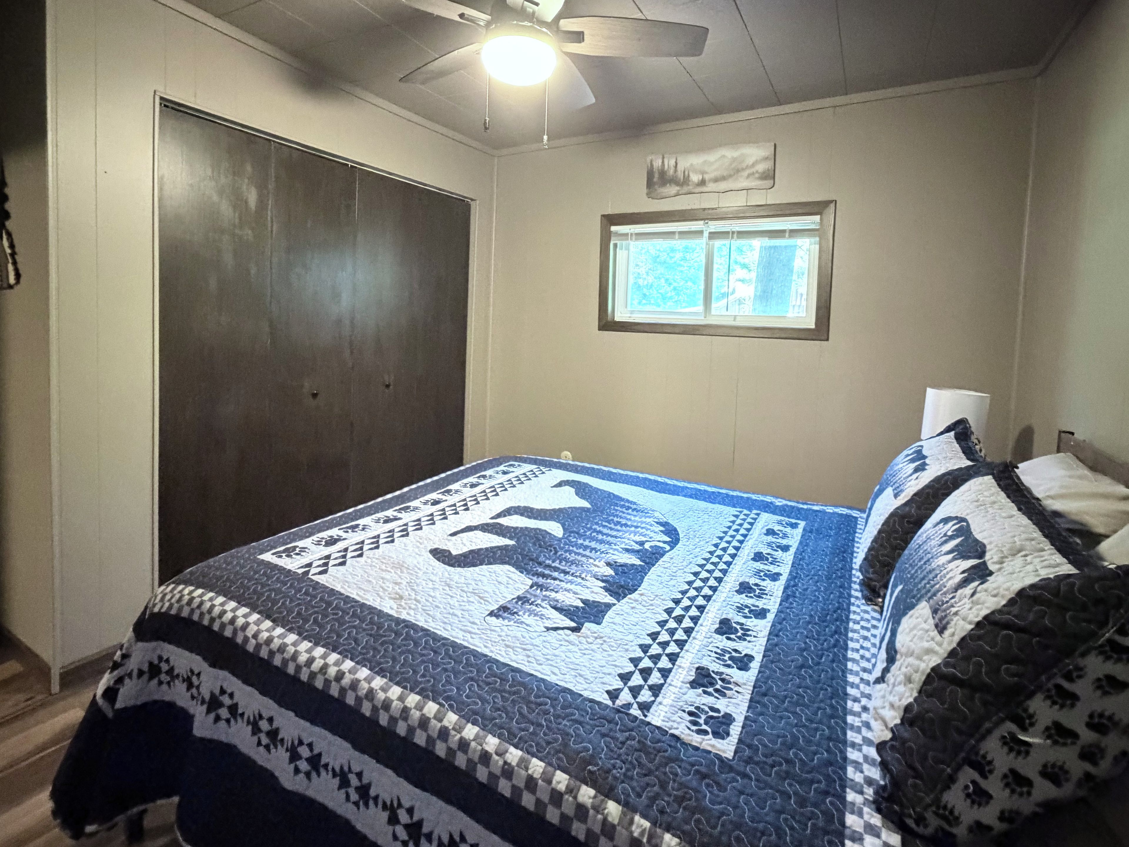Un dormitorio con una cama, ventana, ventilador de techo y puerta.