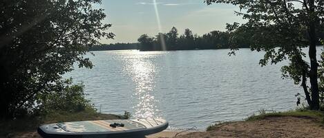 A sandy beach with a paddleboard and a calm lake in the background.