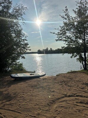 A sandy beach with a paddleboard and a calm lake in the background.