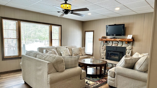 A living room with a beige sofa set, a fireplace, a television mounted above it, and a ceiling fan.