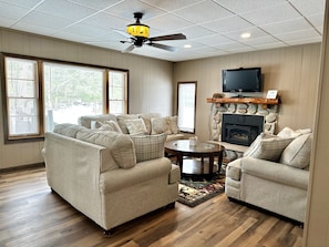 A living room with a beige sofa set, a fireplace, a television mounted above it, and a ceiling fan.