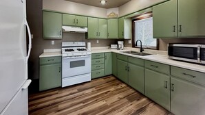 A kitchen with green cabinets, a white stove, a microwave, and a wooden floor.