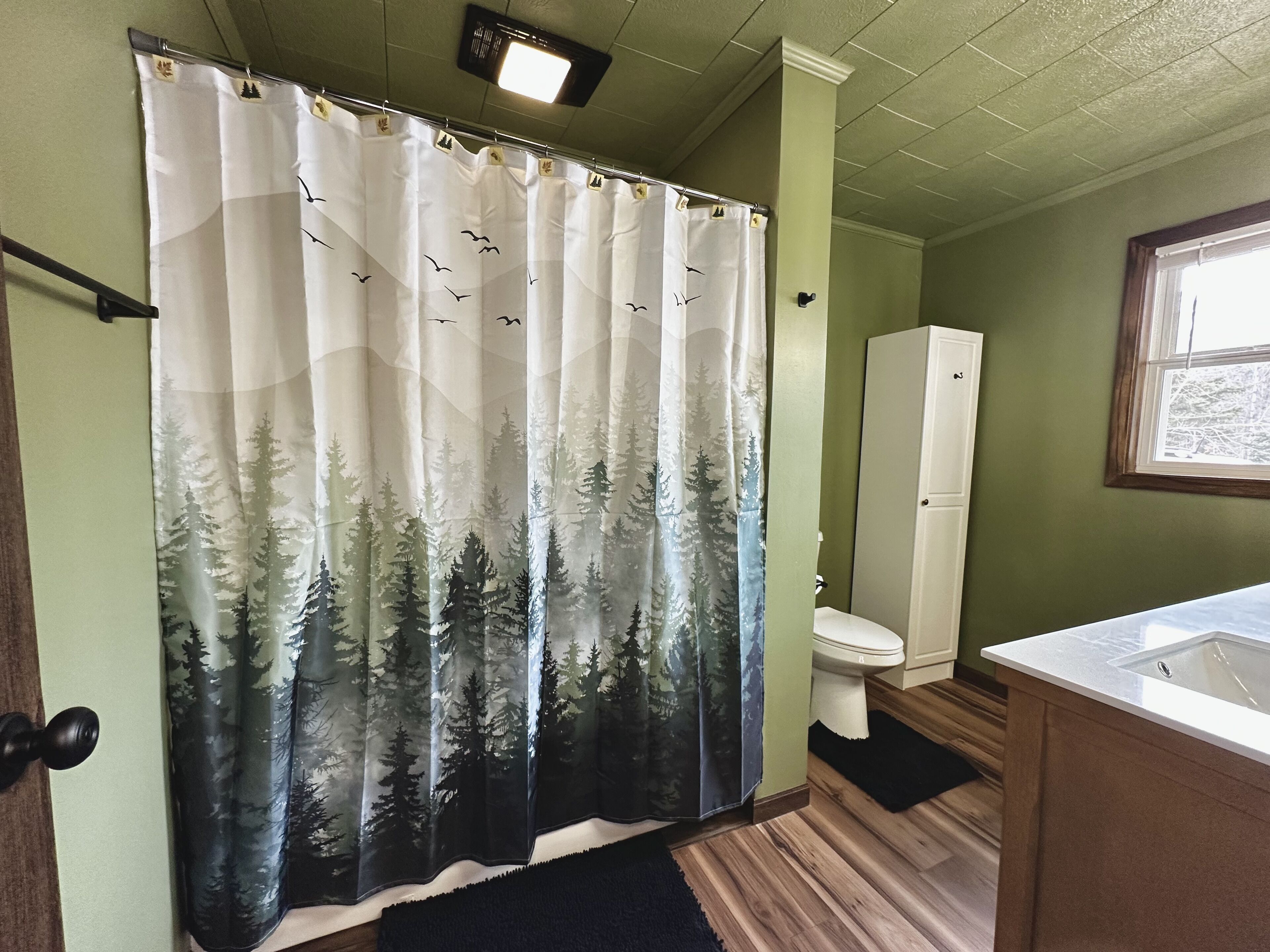 A bathroom with a shower curtain featuring a forest and birds design, a toilet, and a sink.