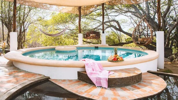 A hot tub with a brick surround, a hanging chair, and a table with fruit. - Remote Beach Eco-Dome w/pool. Near Roca Blanca (Oax.)