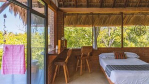 Quarto com cama, escrivaninha e cadeiras, com vista para o verde lá fora.