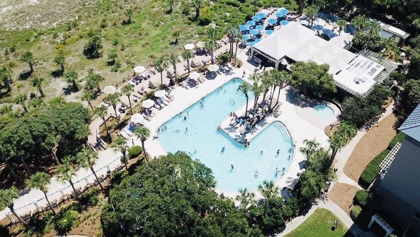 Vista aerea di un resort con una grande piscina circondata da palme e aree relax.