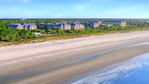 Un hotel sulla spiaggia con diversi edifici, una spiaggia sabbiosa e una vista limpida sull'oceano.