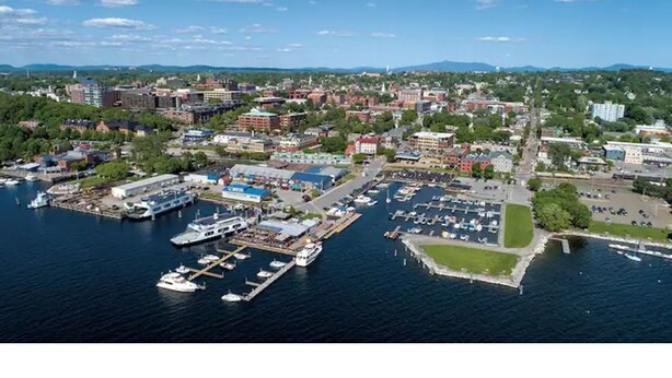 Vue aérienne d’une marina avec des bateaux amarrés, un grand ensemble d’immeubles et une végétation luxuriante environnante.