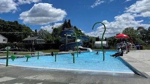 Une piscine avec un toboggan et un parasol rouge.
