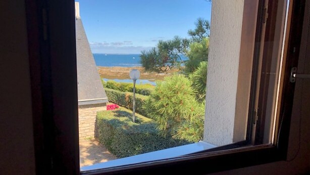 On peut voir, à travers une fenêtre, un jardin, un ciel dégagé et, au loin, la mer.