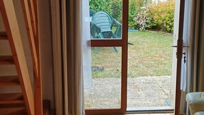 Une pièce dotée d’un escalier en bois, d’une porte-fenêtre coulissante donnant sur un jardin et d’un sol carrelé.