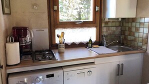 Une cuisine compacte équipée d’un lave-linge, d’une machine à café et d’une fenêtre donnant sur la verdure.