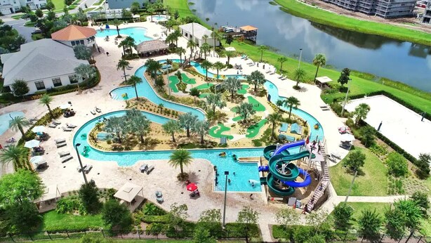 An aerial view of a resort with a large pool area, a water slide, and surrounding greenery. - *Amazing 4Bdr TH*15mins to Disney*Free Amenities! (Kissimmee)