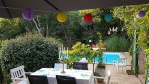 Eine Terrasse im Freien mit Esstisch, umgeben von üppiger Vegetation und einem Schwimmbecken.