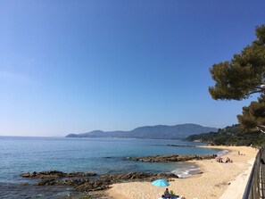 Escena de playa costera con cielos despejados, costa rocosa y montañas a lo lejos.