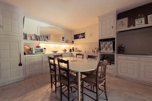 Une cuisine avec des meubles blancs, une table à manger avec des chaises et un four à micro-ondes posé sur le plan de travail.